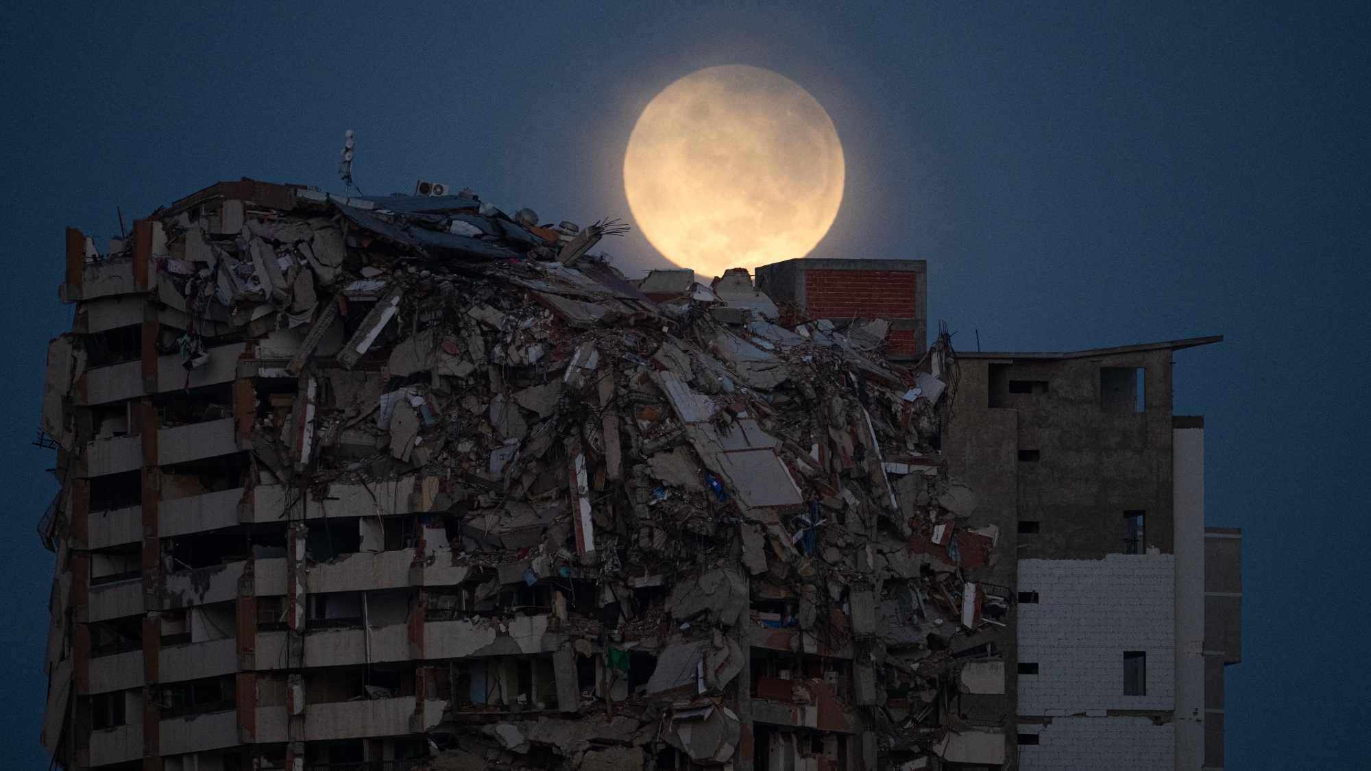 A full moon is seen behind a collapsed residential building in Catia La Mar, La Guaira State, Venezuela, on August 28, 2026, over two months after earthquakes struck the area.