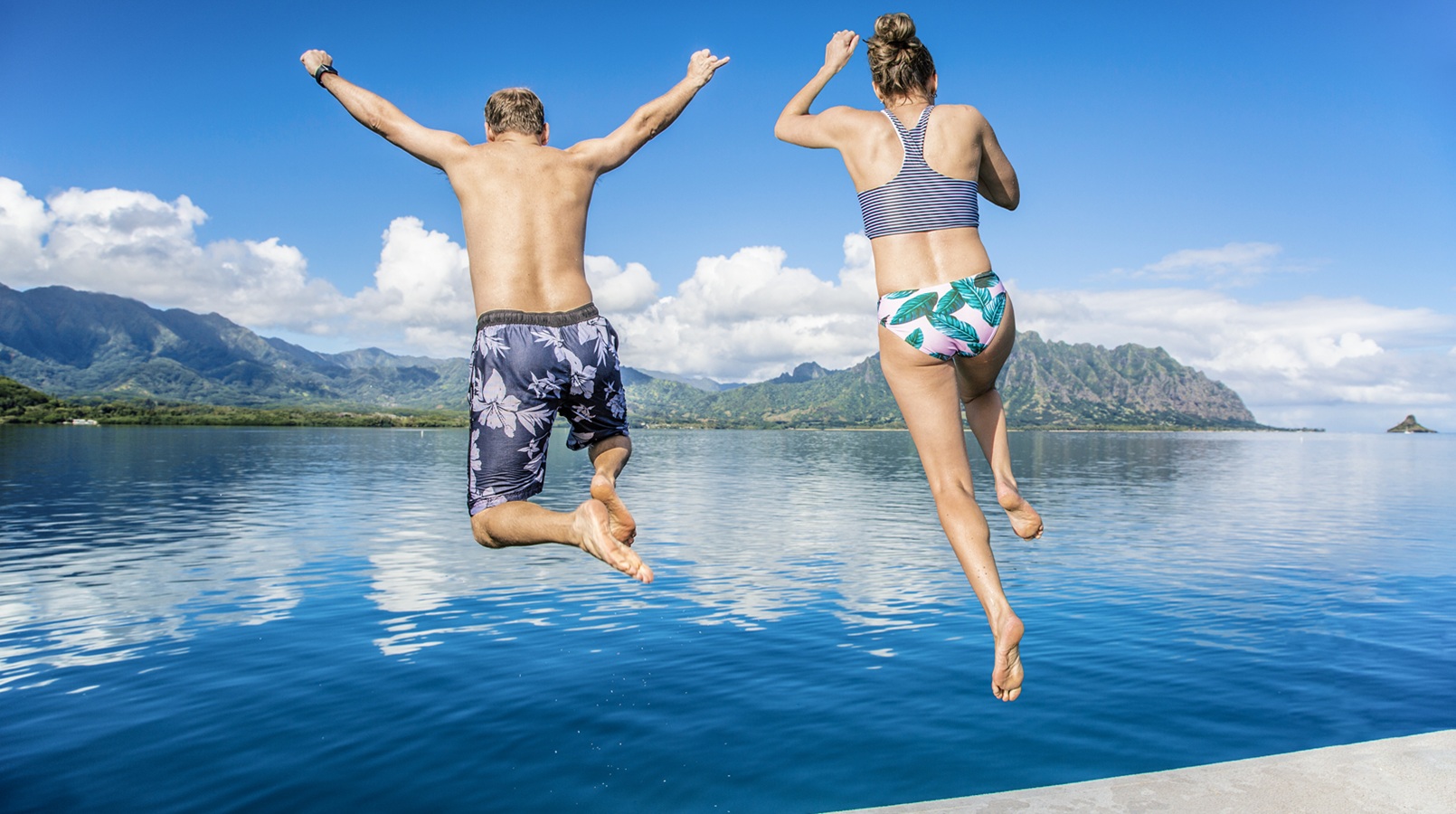 Man and women jumping together into the ocean while on a beautiful scenic Hawaiian vacation. Thrilling and exciting experience. Concept about holiday, success, accomplishment and lifestyle