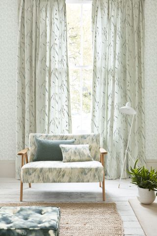 living room curtains with leaf print and pale wallpaper, white wooden floors, coir rug, upholstered retro armchair