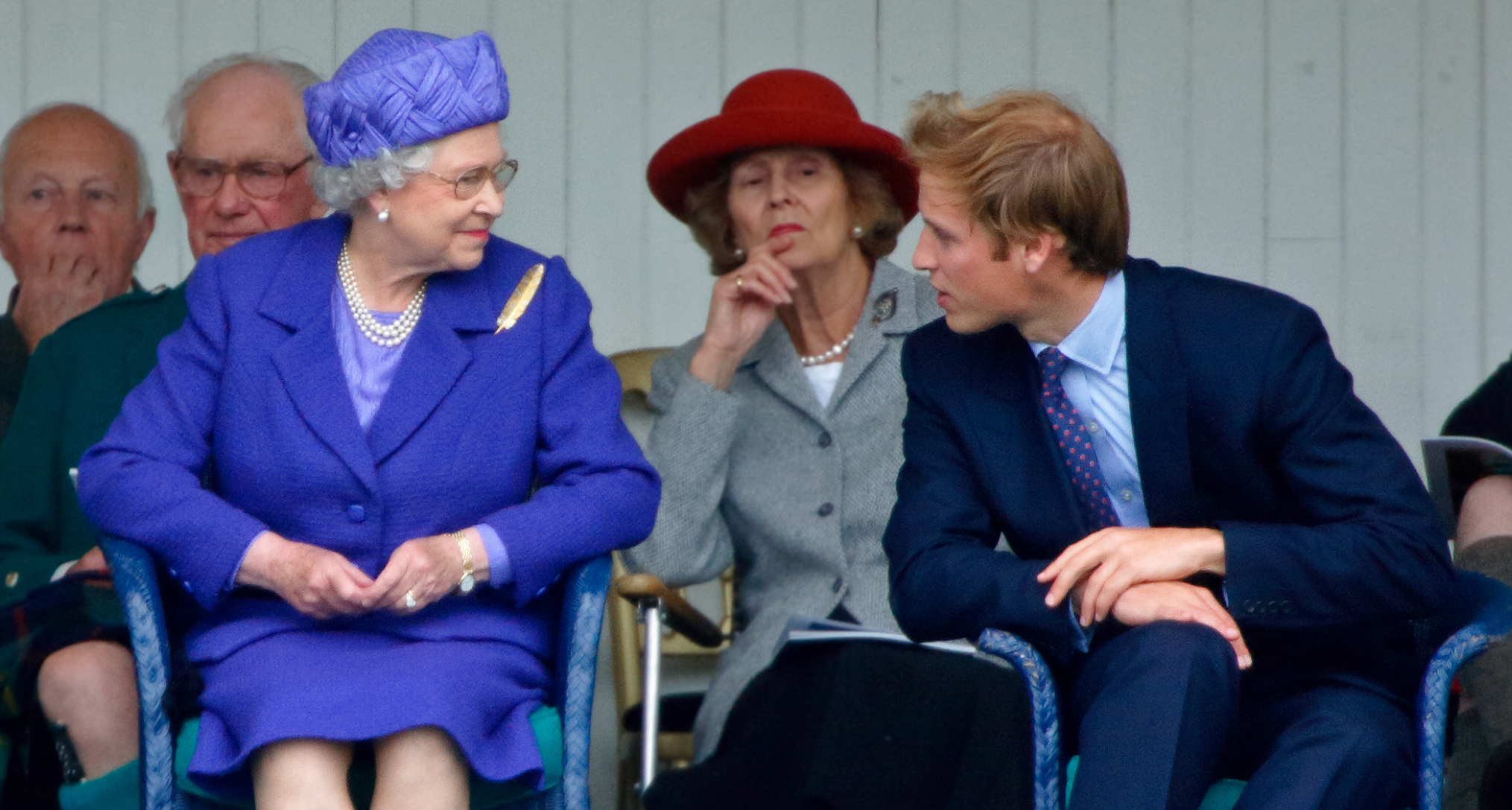 Queen Elizabeth wearing a purple suit sitting next to Prince William and smiling 