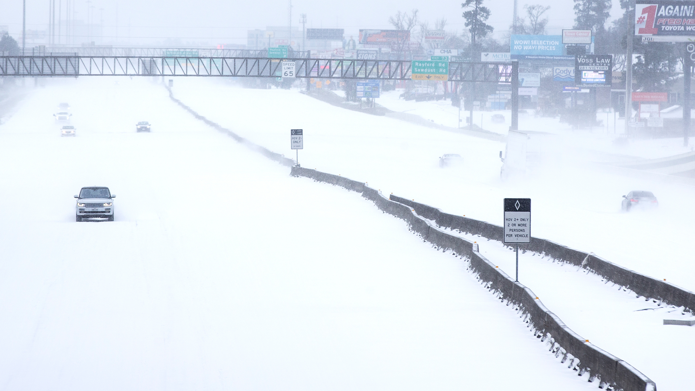 A few cars drive along a snowy interstate along a strip mall in Texas.