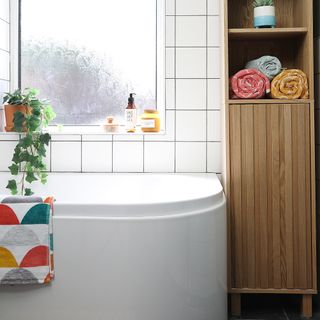 Bathroom with white tiles and bath and wooden towel storage