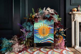 art deco design A rainbow colored cabinet on an art deco rug styled with colorful dried flowers cascading across the cabinet