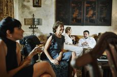 A wealthy family relaxes in a living room with old art on the walls.