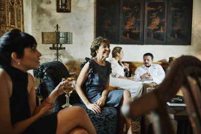 A wealthy family relaxes in a living room with old art on the walls.