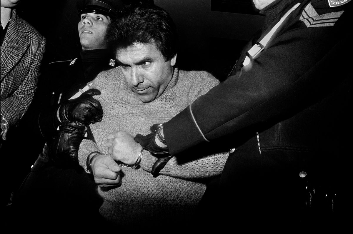  Black and white photograph of a man with handcuffed wrists and held by two police officers