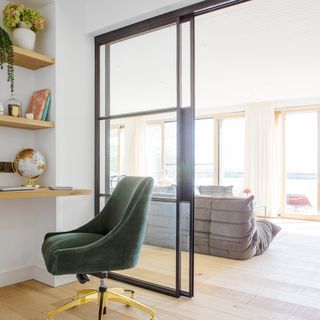 Desk chair and desk in a home office with glass wall and door through to living room