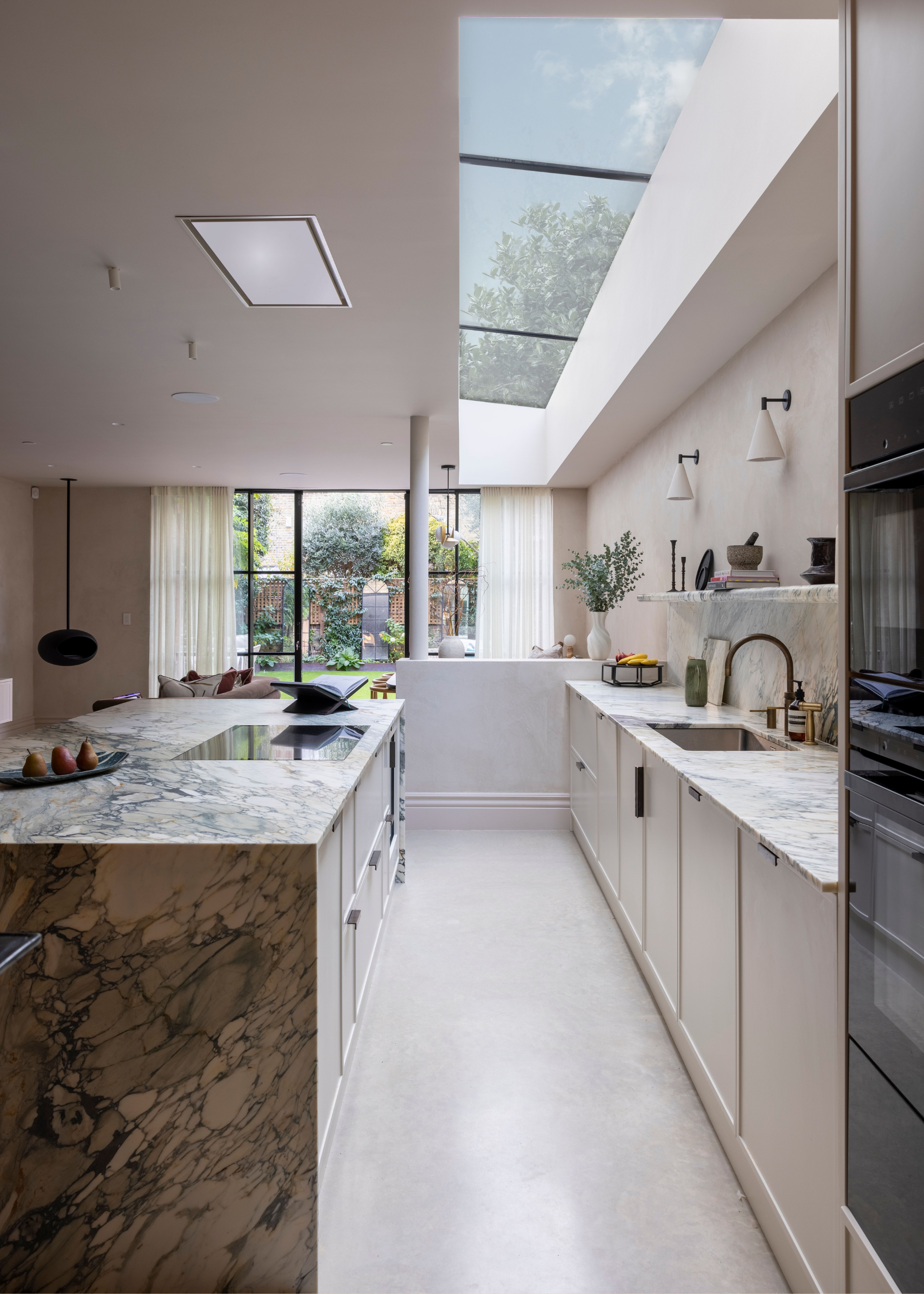 A white and marbles kitchen with cabinet and drawers as well as a large long and narrow skylight built into the ceiling