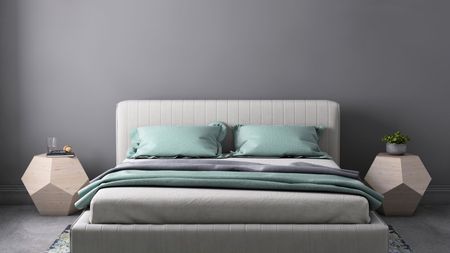 A mattress dressed in gray and green sheets against a gray wall.