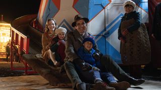 Laura Main as Shelagh and Stephen McGann as Dr Turner sit at the bottom of a helter skelter with Angela (Alice Brown), Teddy (Edward Shaw) and May (April Rae Hoang) Turner in the Call the Midwife Christmas Special 2024.