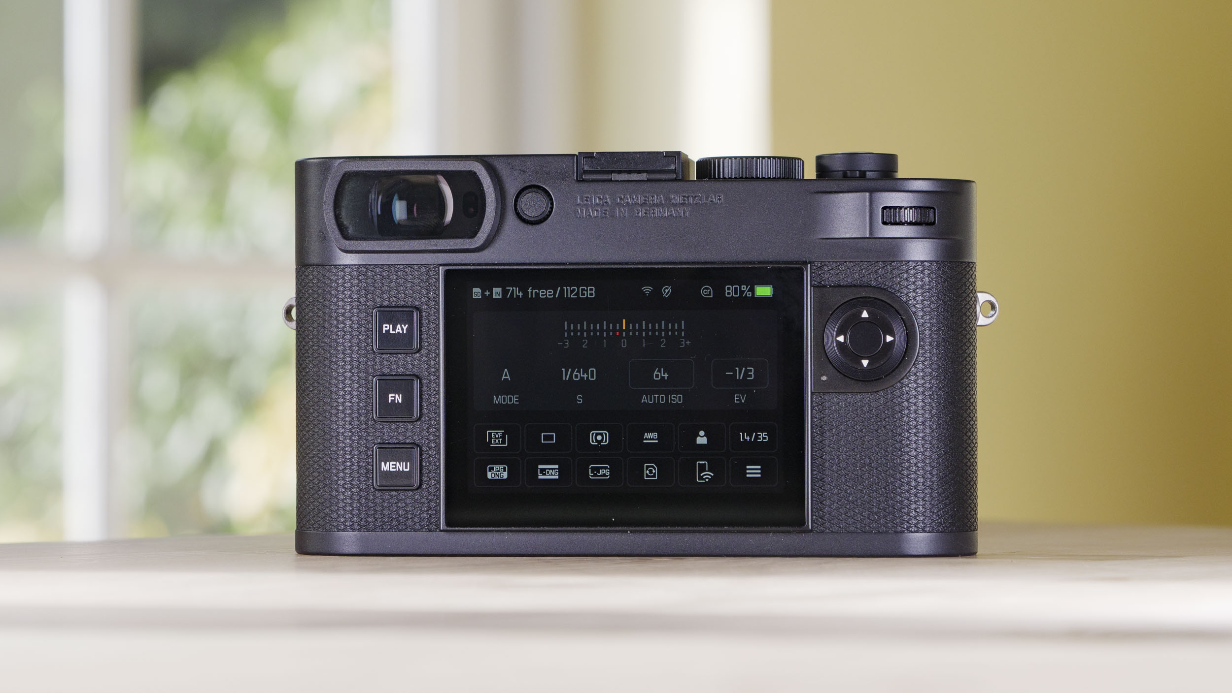 Rear screen of the Leica M EV1 camera on a wooden table with glass-panelled door backdrop