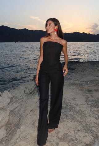 a photo of a woman's spring vacation outfit with shell earrings and black tube top and black trousers