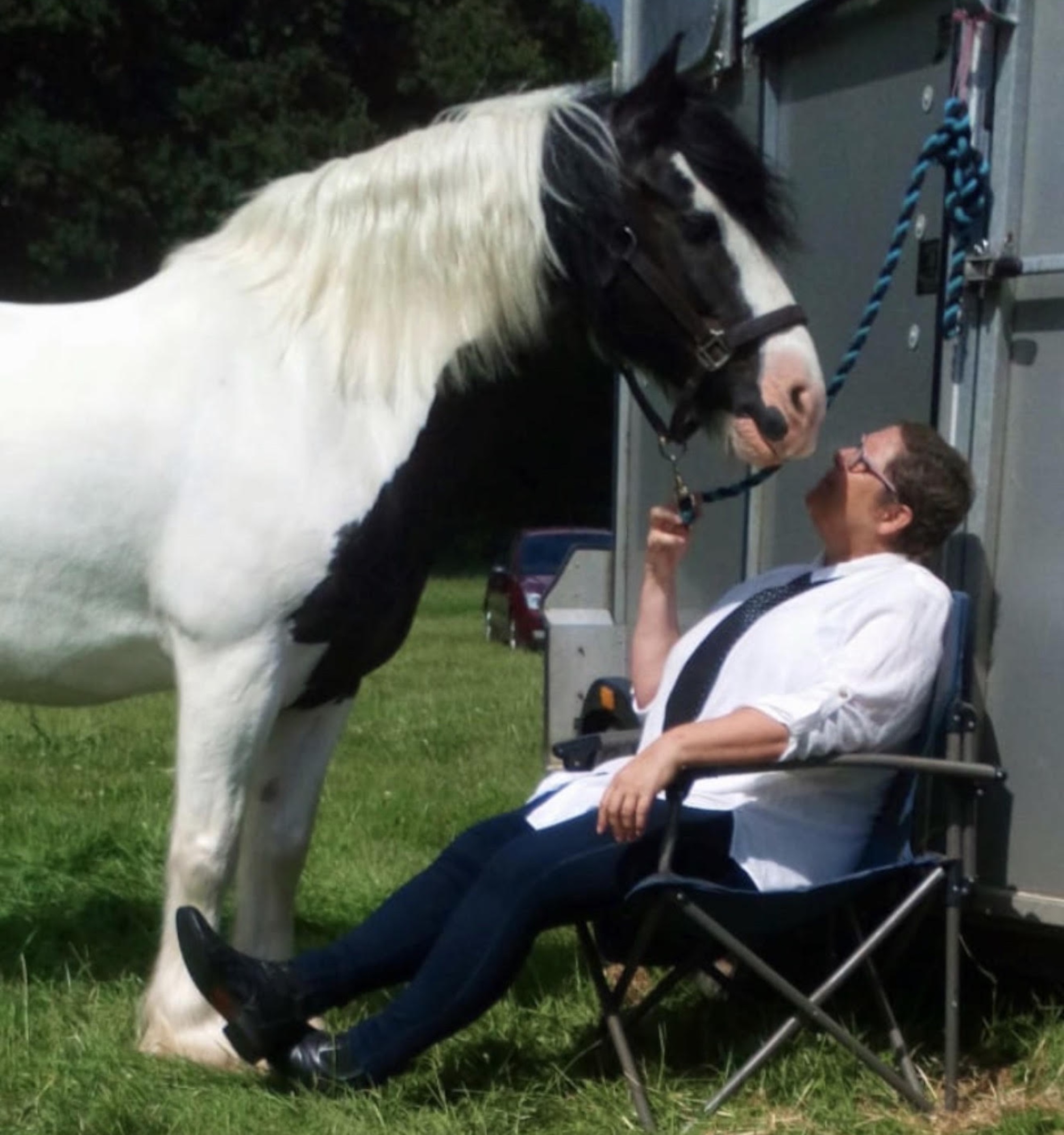 Sally sitting in a chair, looking up at her piebald horse Dexter