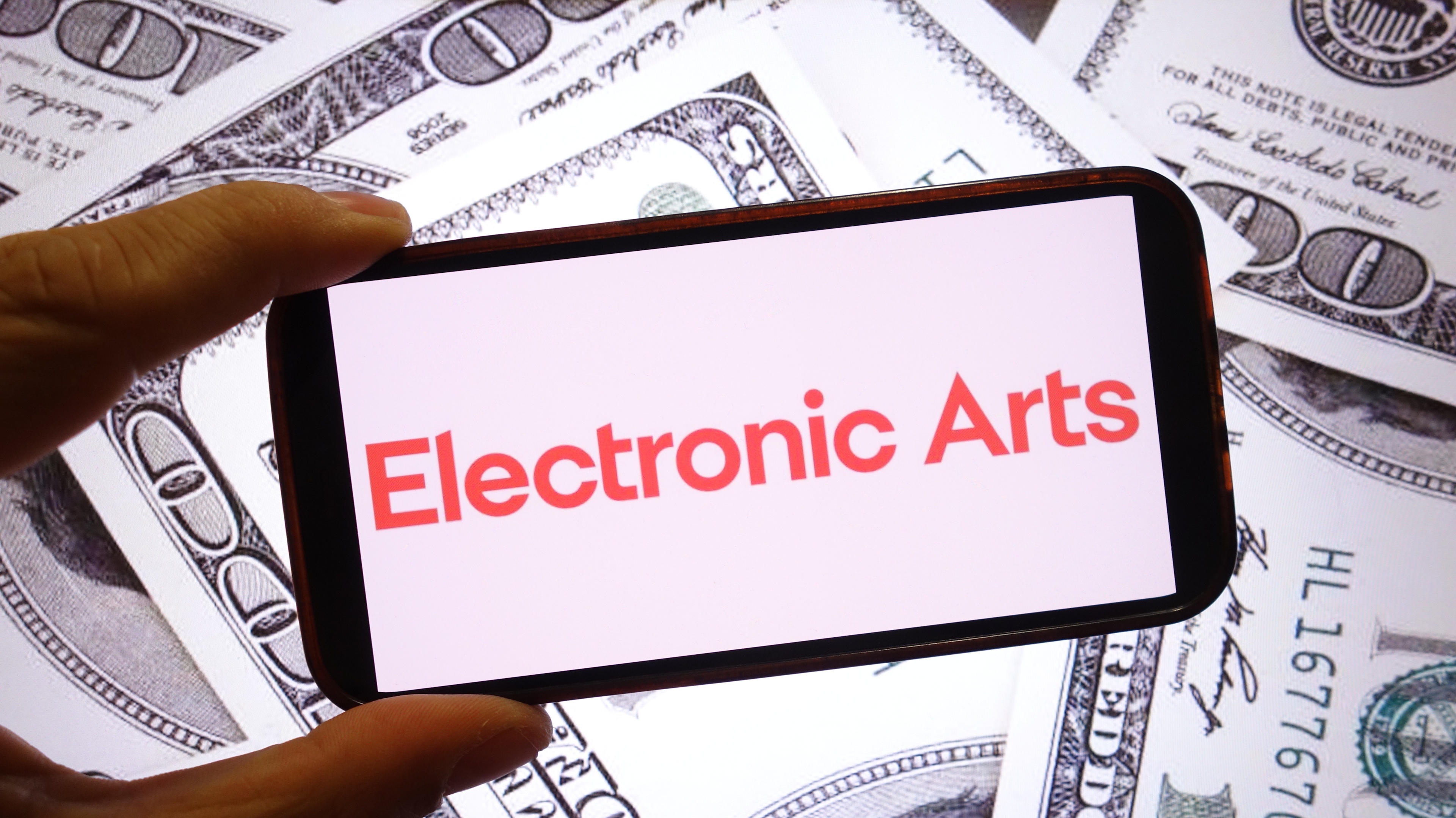 POLAND - 2025/09/28: In this photo illustration, the Electronic Arts company logo is seen displayed on a smartphone screen with United States dollar banknotes in the background. (Photo Illustration by Piotr Swat/SOPA Images/LightRocket via Getty Images)