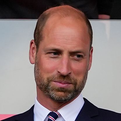 Prince William wearing a suit and tie in front of a pink and white background