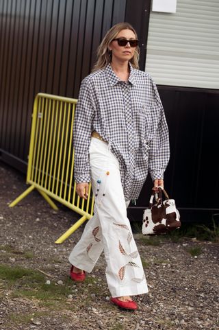 Copenhagen fashion week showgoer wearing plaid shirt, white pants, red ballet flats, and cow print bag