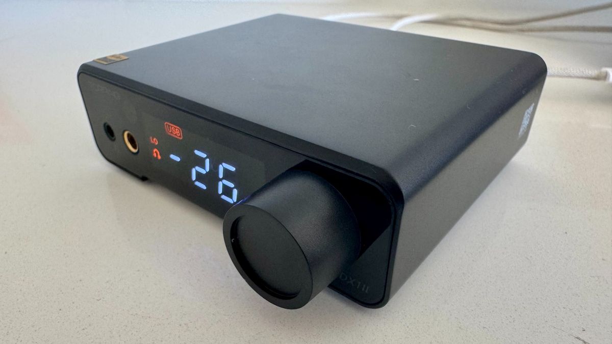 The black Topping DX1 II DAC on, with digital display, on a white surface