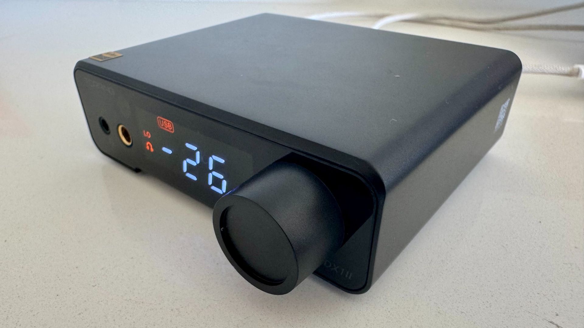 The black Topping DX1 II DAC on, with digital display, on a white surface