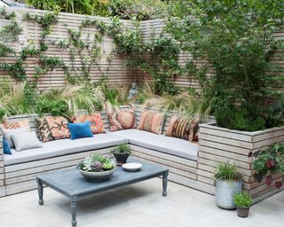 A white and bright backyard corner seating area with a painted fence, a built-in corner sofa, and a blue coffee table