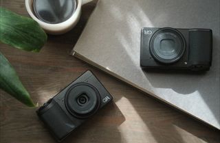 A pair of Ricoh GR III cameras, laying on a table next to a cup of coffee