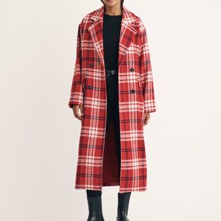 A model wears a red and white Nobody's Child Check Coat over a black top and skirt with boots