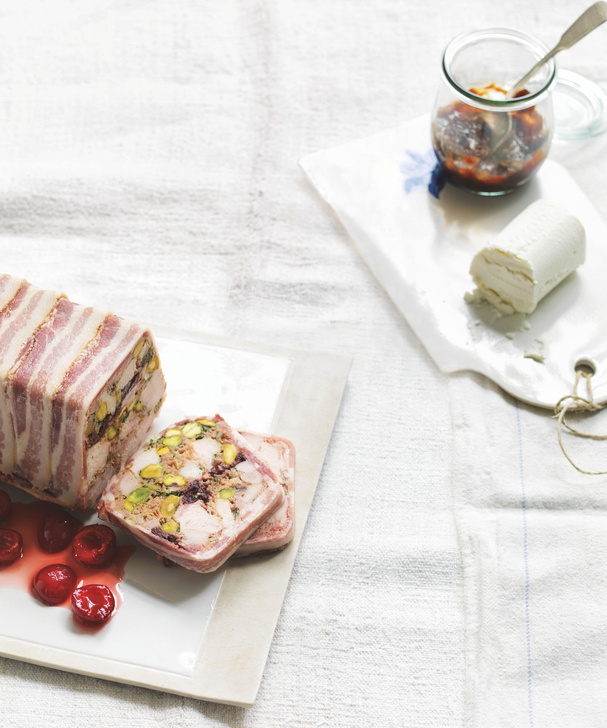 chicken and pistachio terrine which pickled cherries on a white board on a white tablecloth