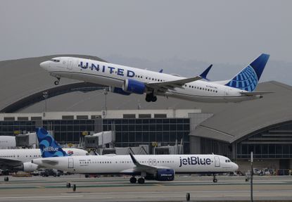 A United Airlines plane taking off from an airport as a JetBlue Airways plane taxis on the runway.