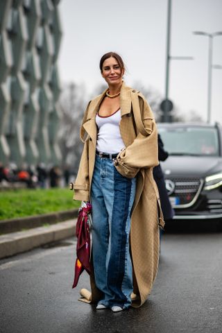 woman wearing a trench coat, a white tank, and jeans