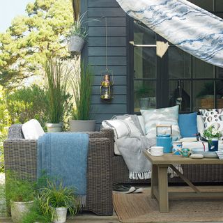 Seating area just outside a black clad house with sofa and armchair covered by garden sail