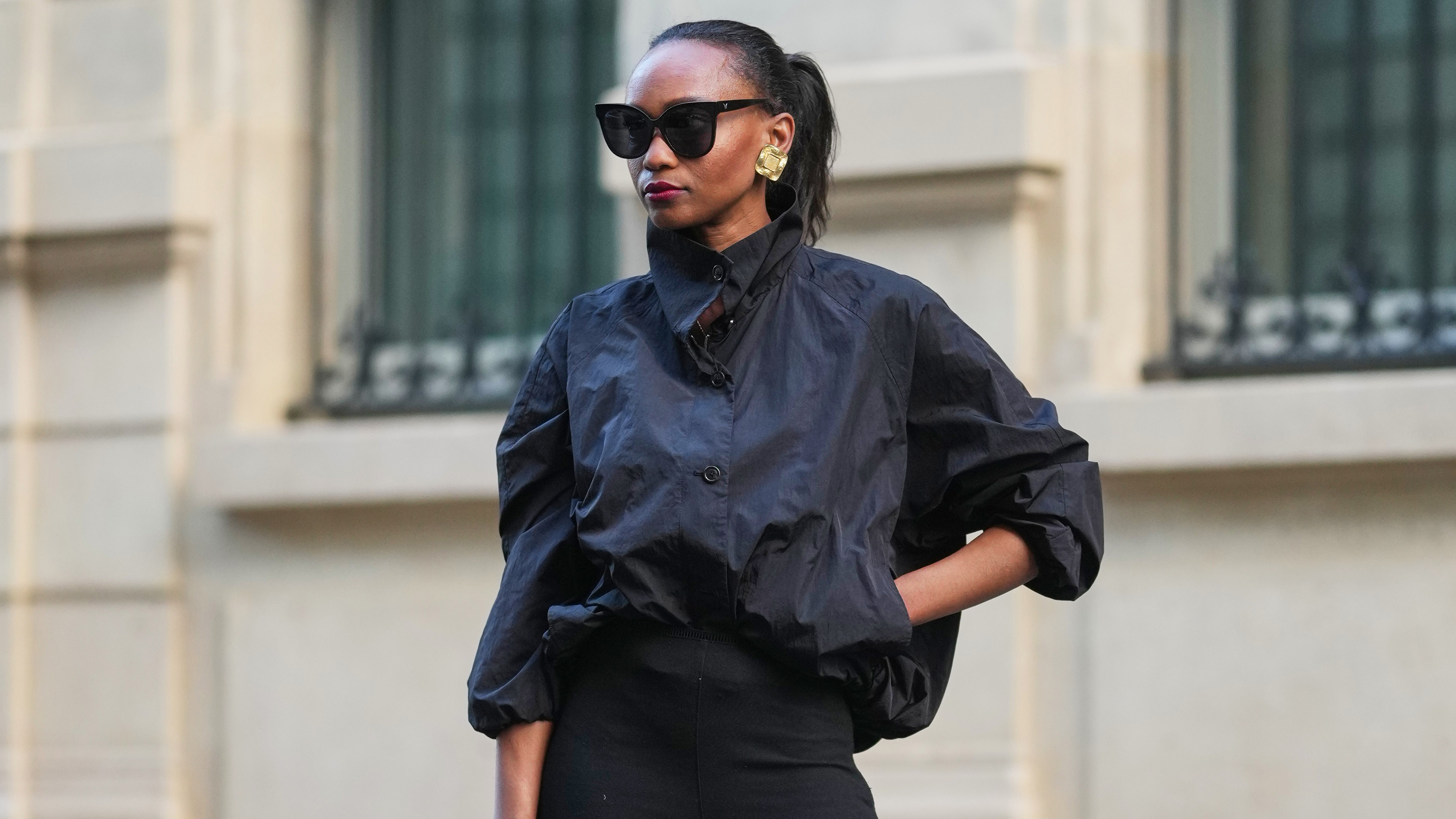 a woman wears a black jacket, sunglasses, and stirrup leggings.
