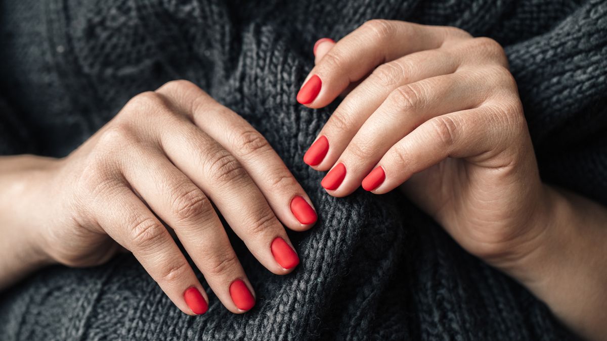 Woman hand with long nails and a bottle of dark red burgundy nail