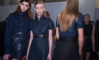 Four female models wearing looks from the Diesel Black Gold collection. One model is wearing a dark blue long sleeve piece with embellishments, a black embellished belt and a short dark blue patterned skirt. Next to her is a model wearing a dark blue quilted effect dress with zip and two black embellished belts. The third model is wearing a dark blue quilted effect piece with short sleeves and a black pleated skirt. And the fourth model is in the background wearing a black sleeveless top and short black embellished skirt