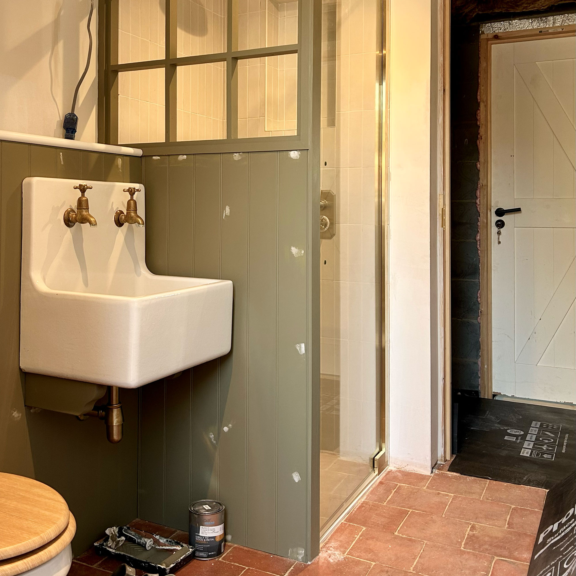 Bathroom mid-renovation with shower enclosure walls and glass door in place, plus country style sink and terracotta floors
