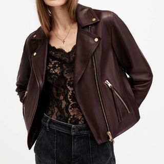 A model wearing an All Saints Dalby Slim Fit Biker Jacket in Oxblood over a lace vest and jeans