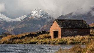 A boat house on a loch with the snow covered Arrochar Alps in the background