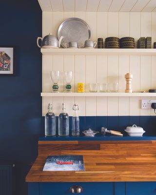 Deep blue kitchen walls, a white wall and shelf and cherry wood worktops.