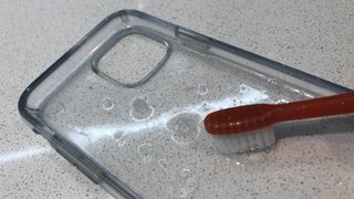 A clear phone case being cleaned with dish soap and a toothbrush