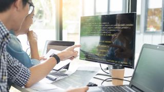 Two people looking at code on a computer monitor