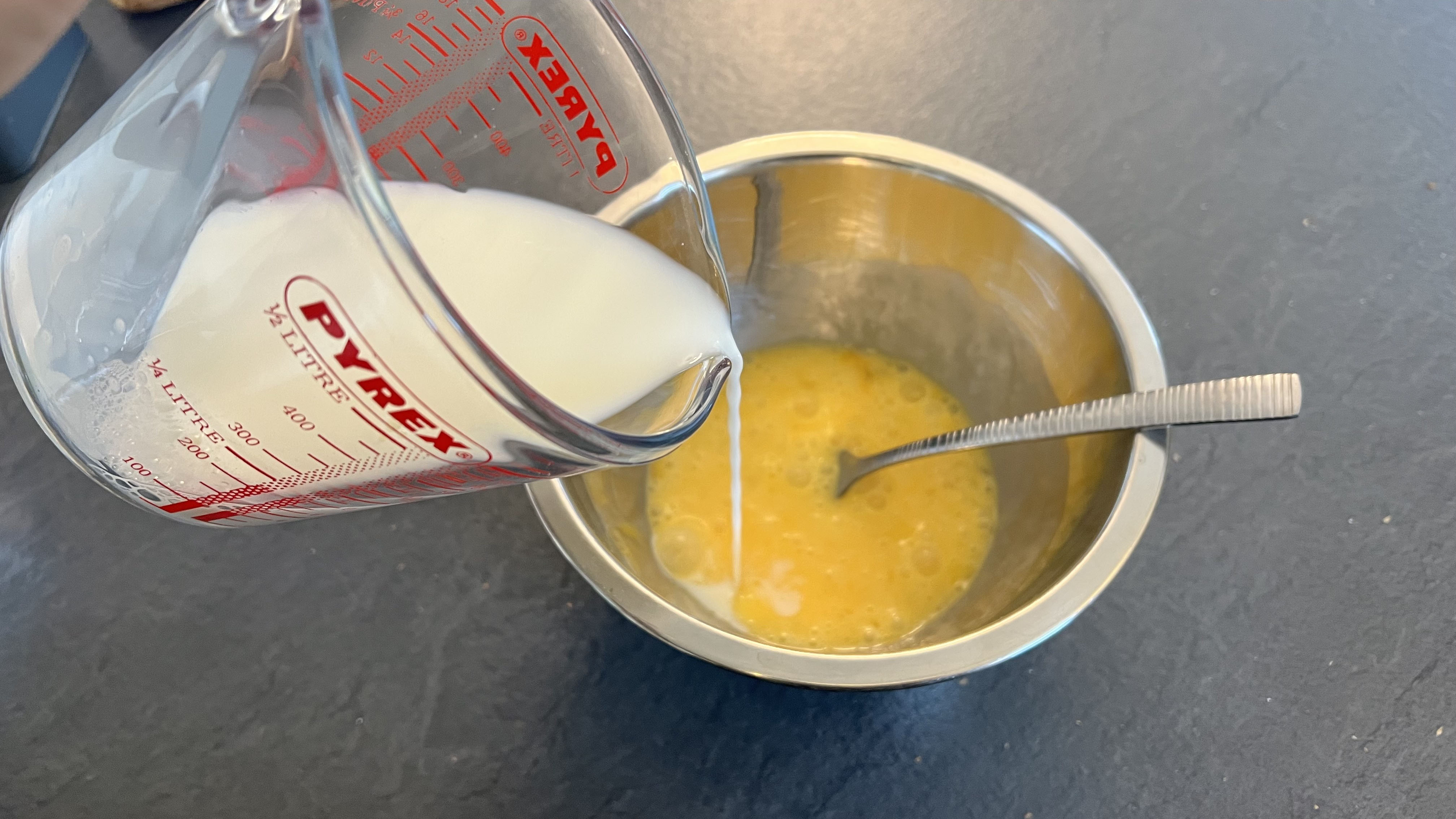 Milk being poured into a bowl with beaten eggs