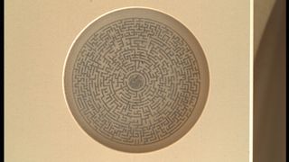 an intricate circular labyrinth inside a metal enclosure with a circular glass window