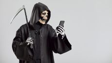 A grim reaper with a scythe, looking at a smartphone in his hand.