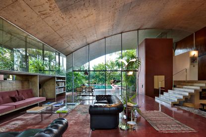 Concrete and glass house with red floor and walls, sofas, glass tables and a view to a pool outside