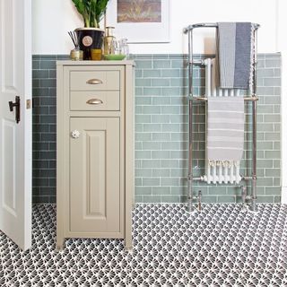 bathroom with pale green metro tile wall, monochrome patterned floor and cream cabinet