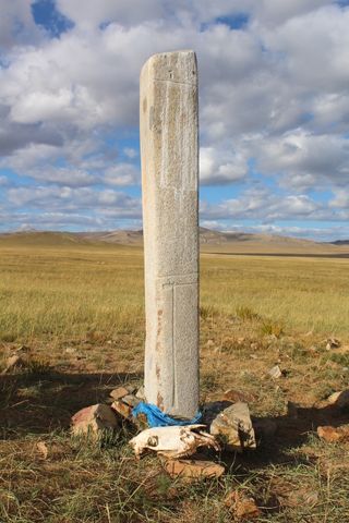 A horse skull and a ceremonial blue prayer scarf sit at the base of a deer stone in central Mongolia.