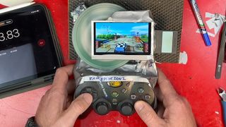 Hands holding PS2 handheld made from Slim console, MadCatz controller, and duct tape woth exposed disc spinning and Classic British Motor Racing gameplay on screen.