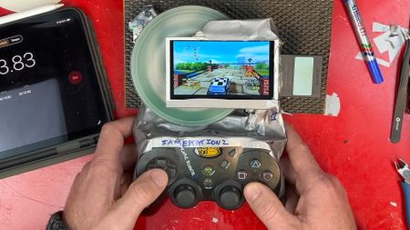 Hands holding PS2 handheld made from Slim console, MadCatz controller, and duct tape woth exposed disc spinning and Classic British Motor Racing gameplay on screen.