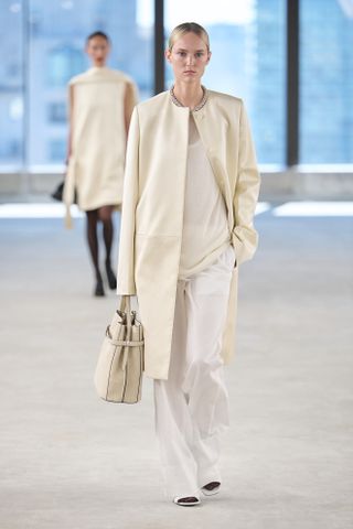 A Toteme model walks the spring/summer 2025 runway wearing a collarless coat.