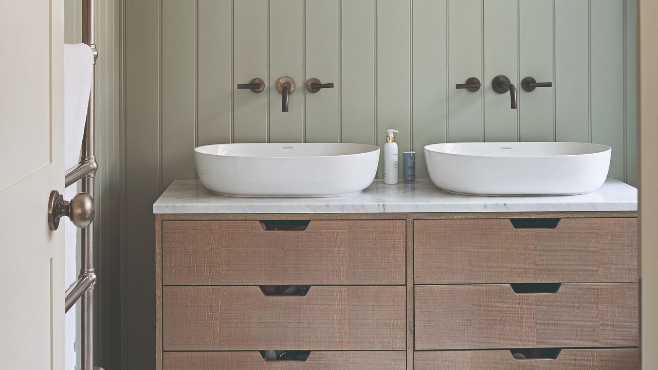 A sage green wall-panelled bathroom with two sinks