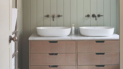 A sage green wall-panelled bathroom with two sinks