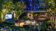 a sunken seating area in a beautiful, well lit garden, with a glass extension behind it